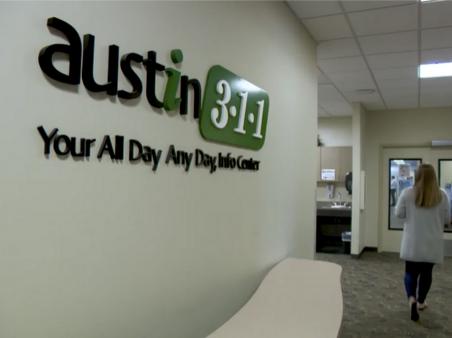 Interior of Austin 3-1-1 building with logo on wall and woman walking