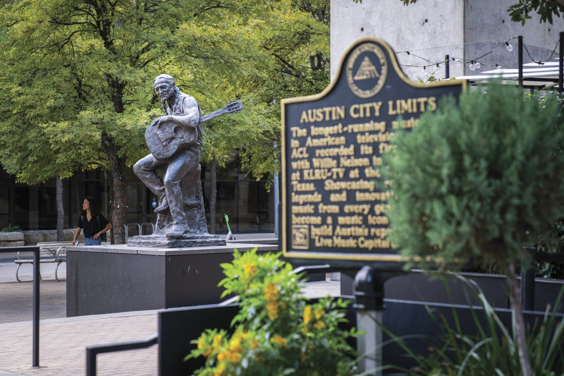 Statue of Willie Nelson with Austin City Limits sign with trees and plants in fram