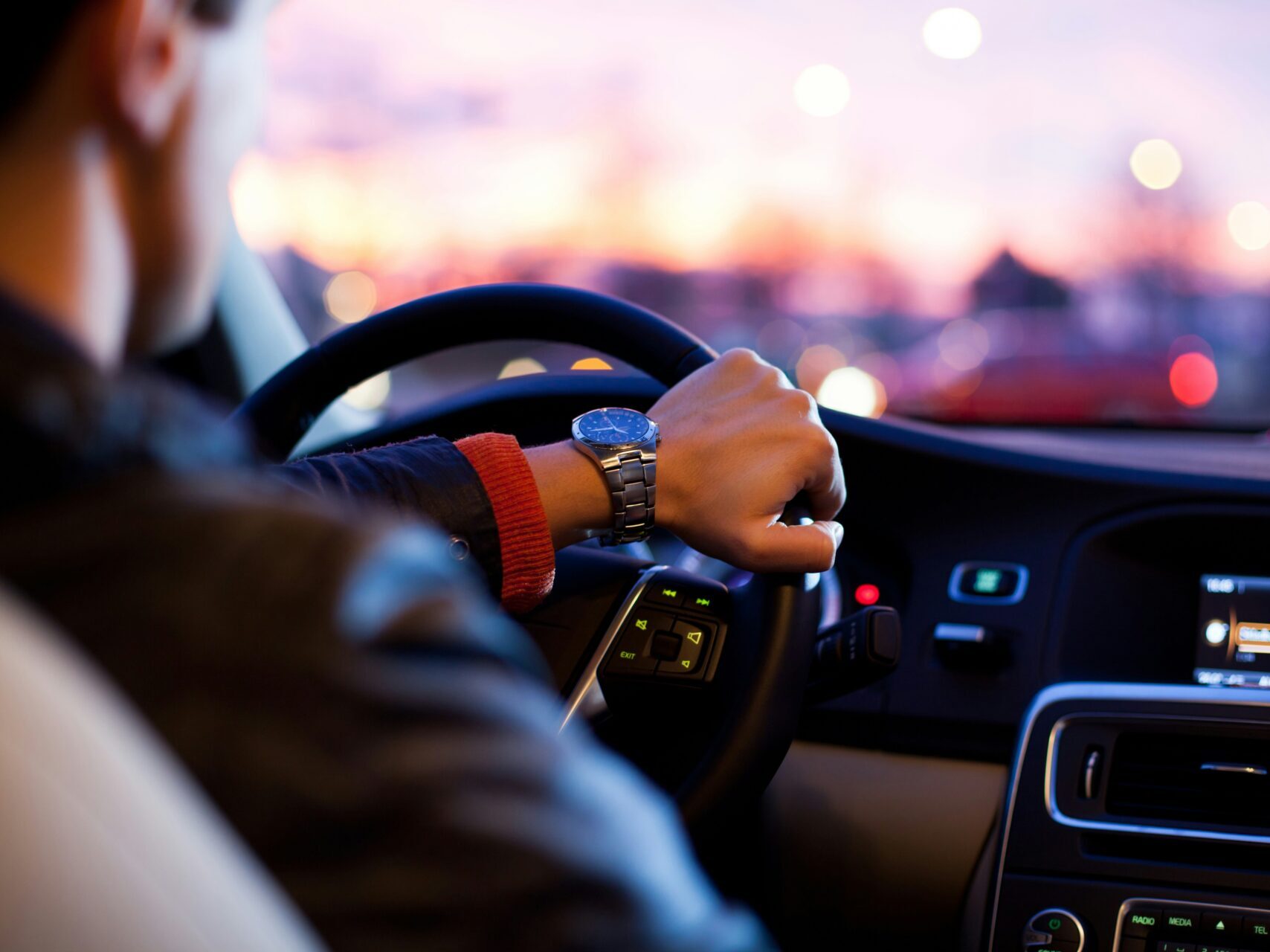 interior image of man driving a car at dawn with pink sky in background
