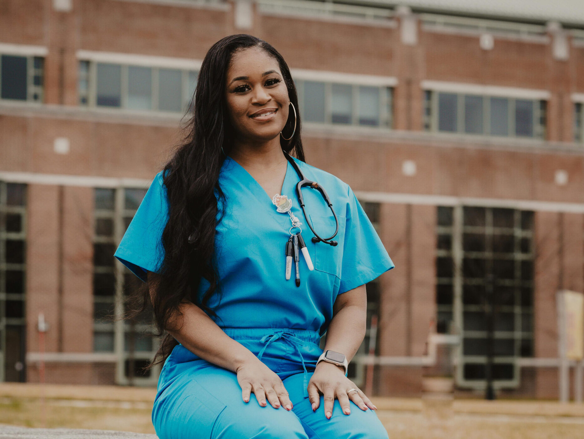 smiling nurse sitting in front of hospital building in scrubs