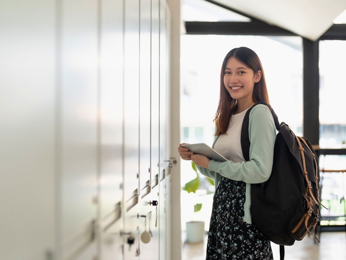 A female high school student standing in front of her school locker holding her books with back pack on - for article Private High Schools in Austin for newcomers moving to Austin.
