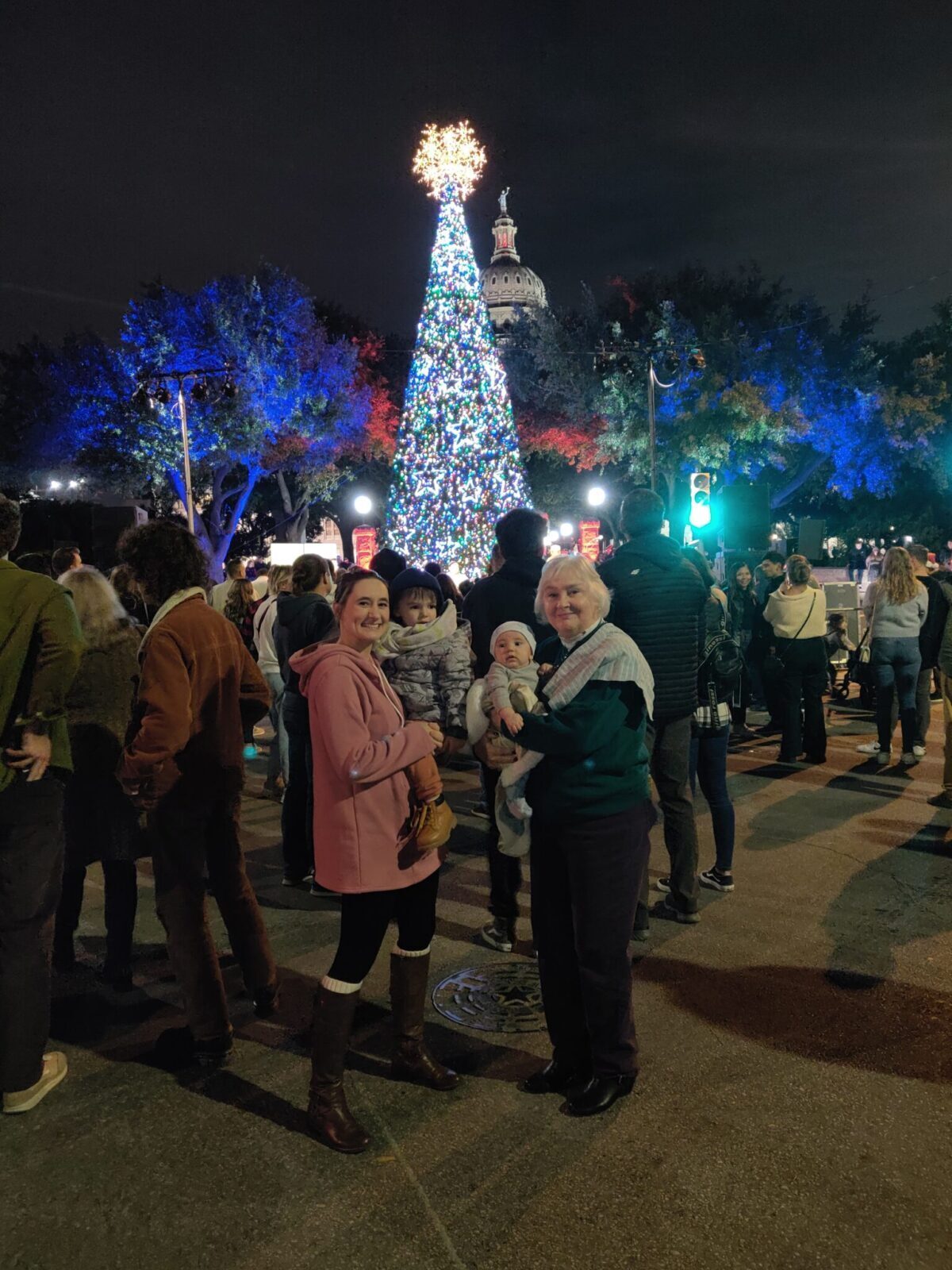 Grandmother, Daughter-in-law, and grandson all standing in front of the tree at the Texas State Capitol.