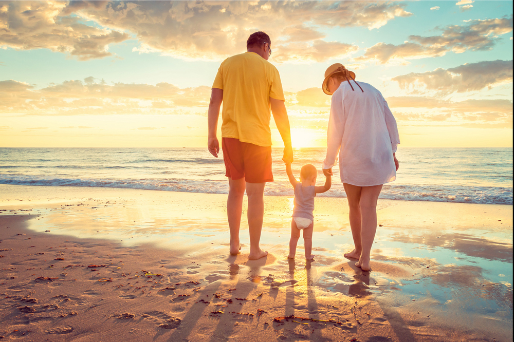 A mom and dad with their kid walking in the beach during a sunset