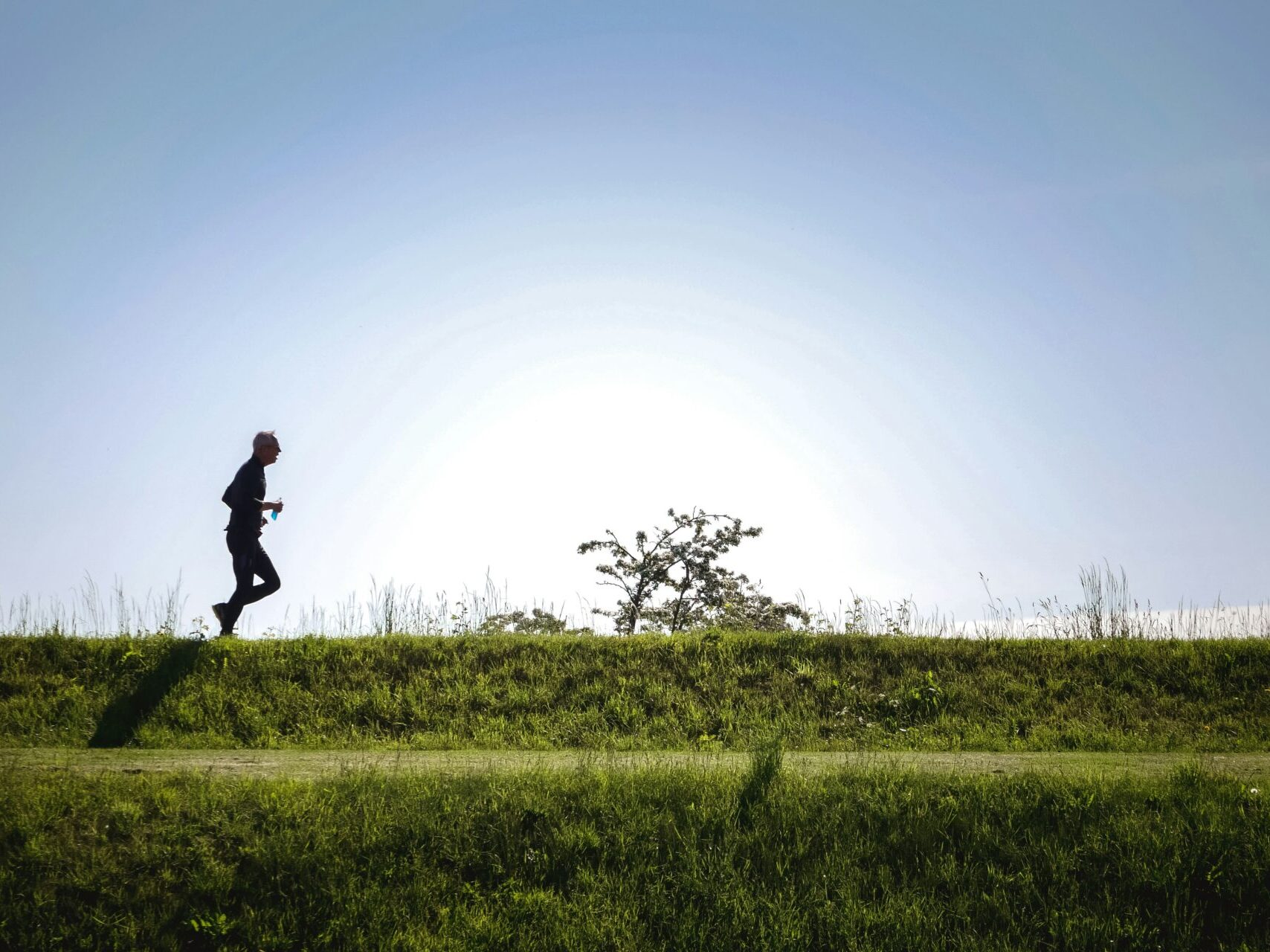man running outdoors with blue sky and grass in foreground