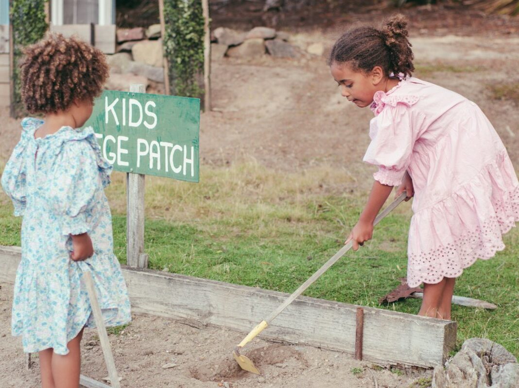 two small girls raking the dirt in a small garden