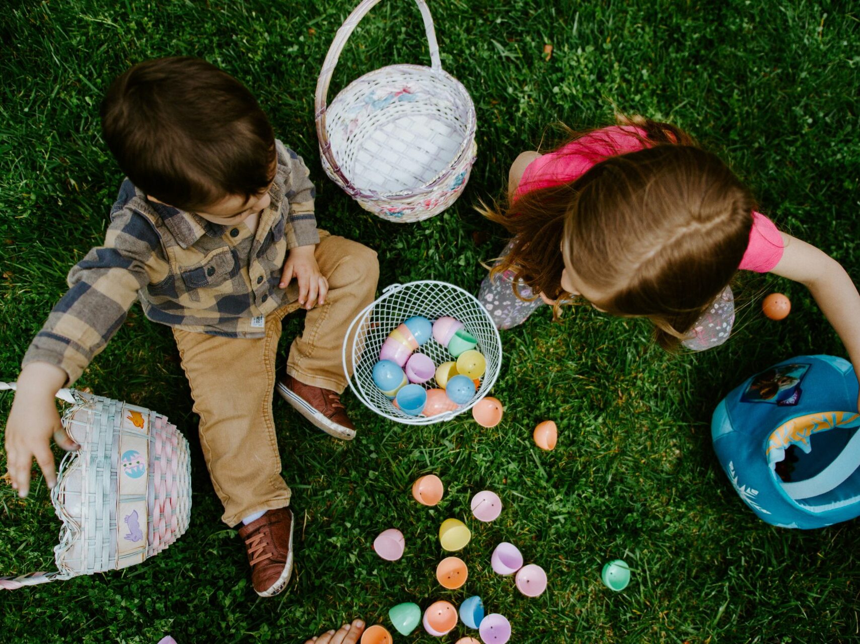 two kids sorting their colorful easter eggs on green grass