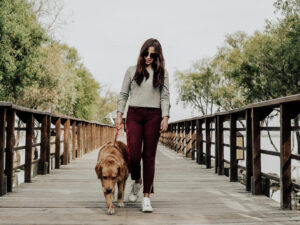 woman in sunglasses walking a dog on a bridge