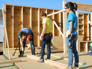 Young people building a wall wearing jeans, safety glasses and tools