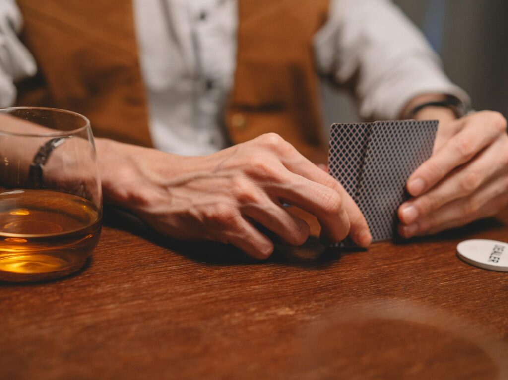 person sitting at wooden table with a clear glass next to them, holding playing cards