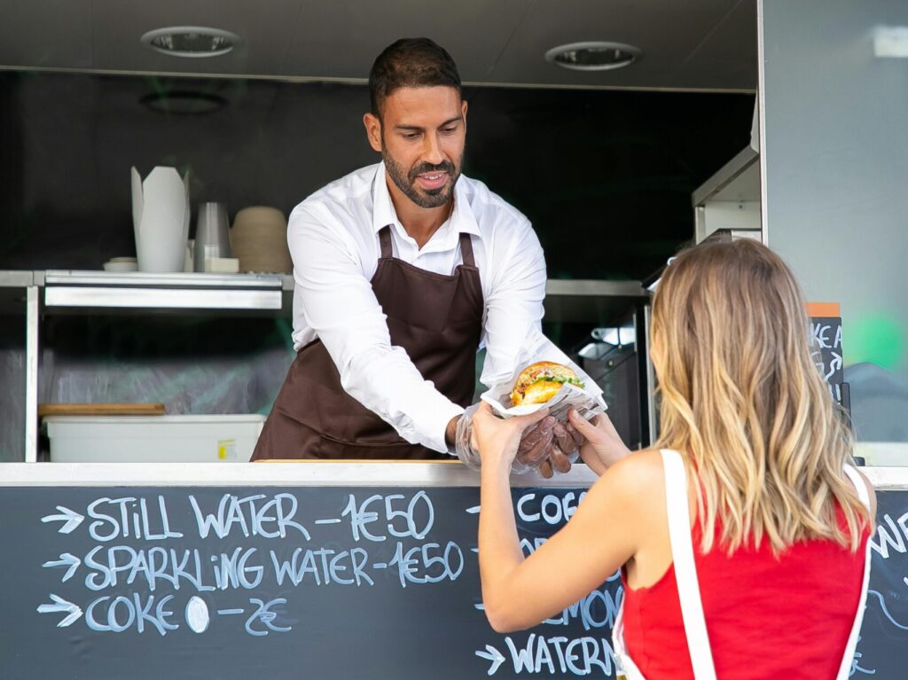 man in food truck serving a woman in red top food through the window