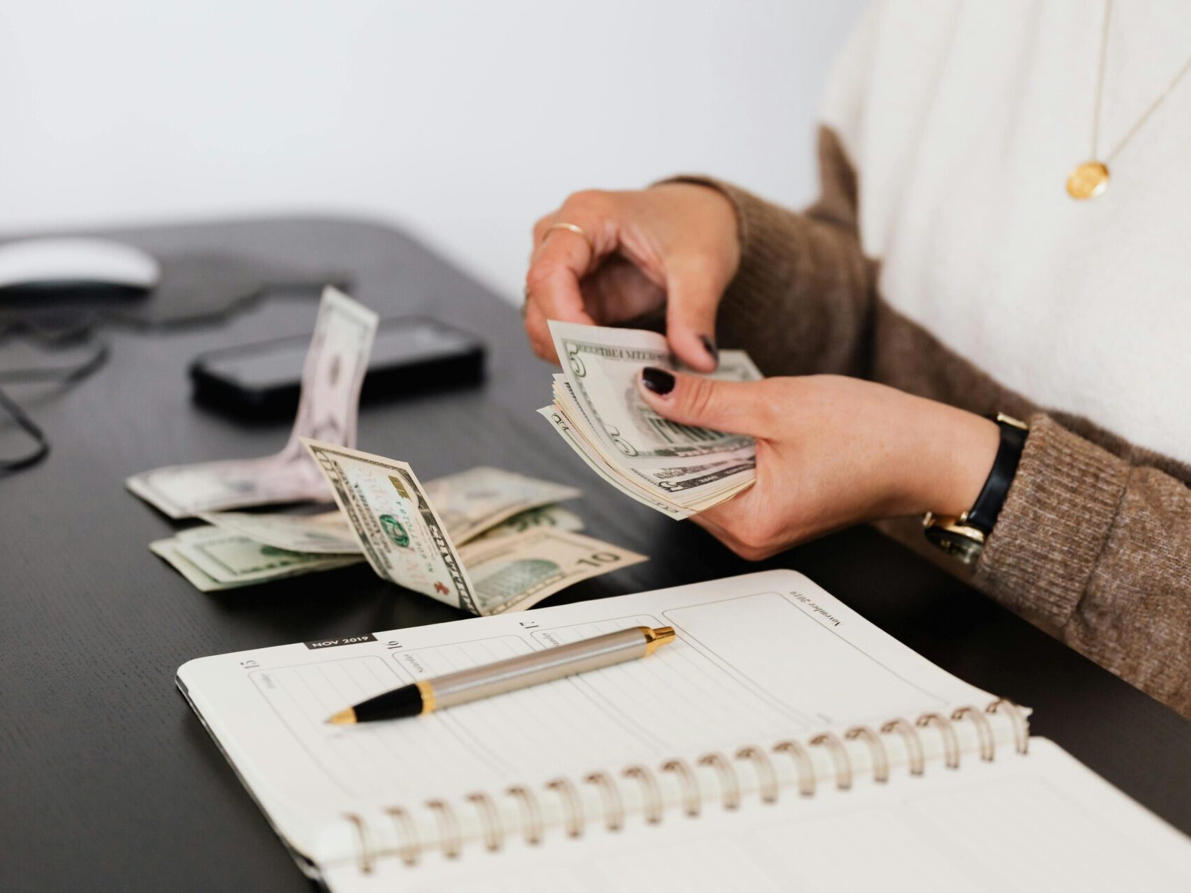 woman sitting at desk counting money over spiral notebook and pen