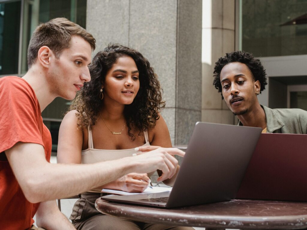 3 adults sitting at table looking at shared laptop