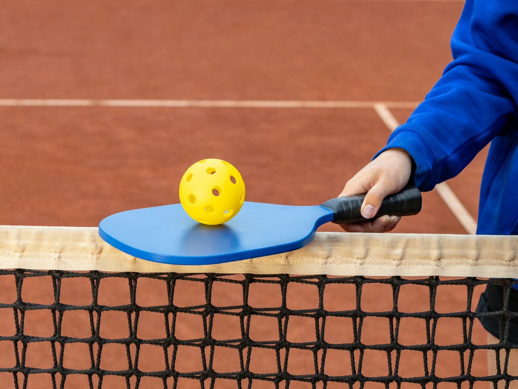 a person holding a pickleball racket balancing a pickleball on top