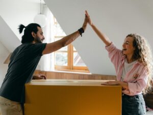 man and woman high fiving each other over a big moving box in the daytime