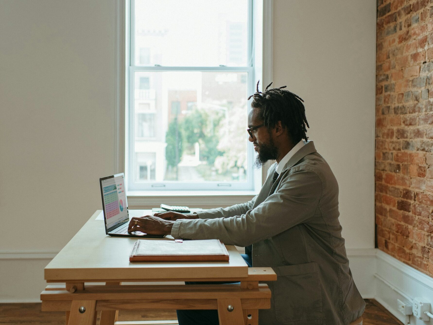 man sitting behind a wood table in a grey suit working on laptop