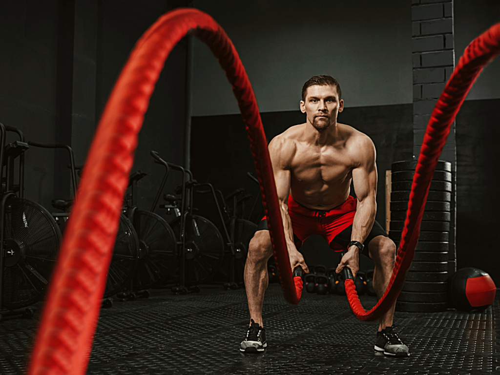 Male at crossfit gym using red battle ropes.