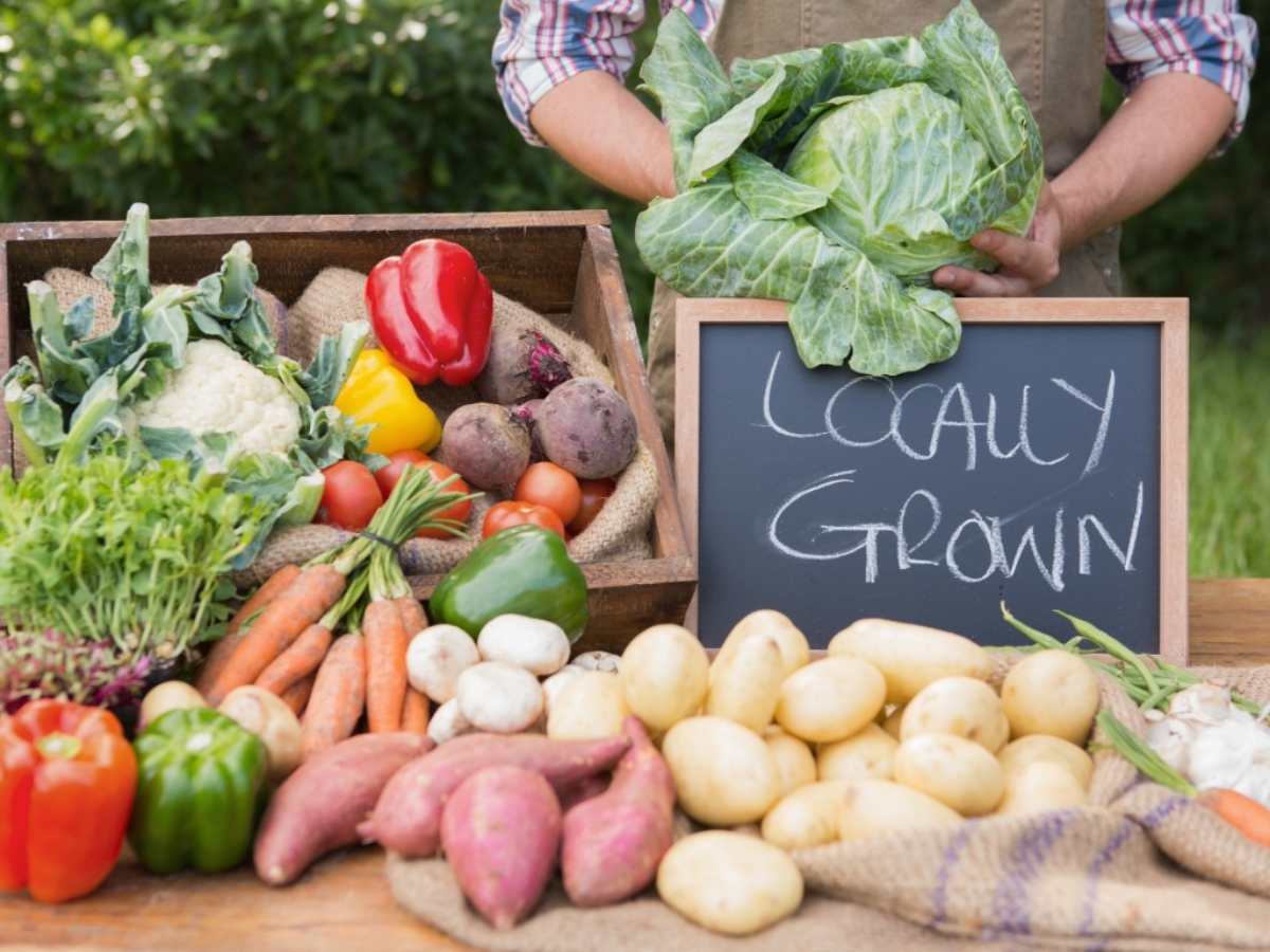 Fresh produce on an outdoor table with a chalkboard sign that says locally grown.