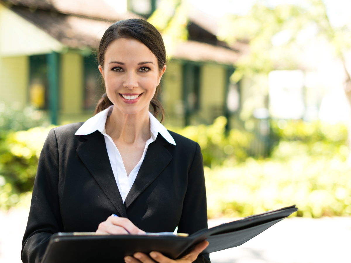 Realtor standing in front of home holding an open notebook.