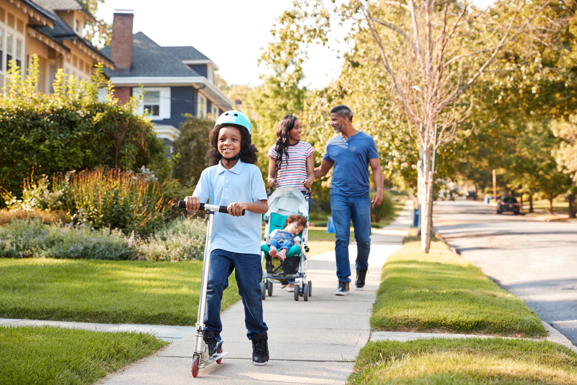 Girl on scooter in front of family walking on sidewalk enjoying neighborhood.