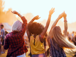 Back of 3 people who are swinging their arms in the air at a fall music festival.