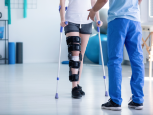 Physical therapy being shown as a person wearing a knee brace walks toward therapist on crutches. This is for the article on Physical Therapy in Austin.