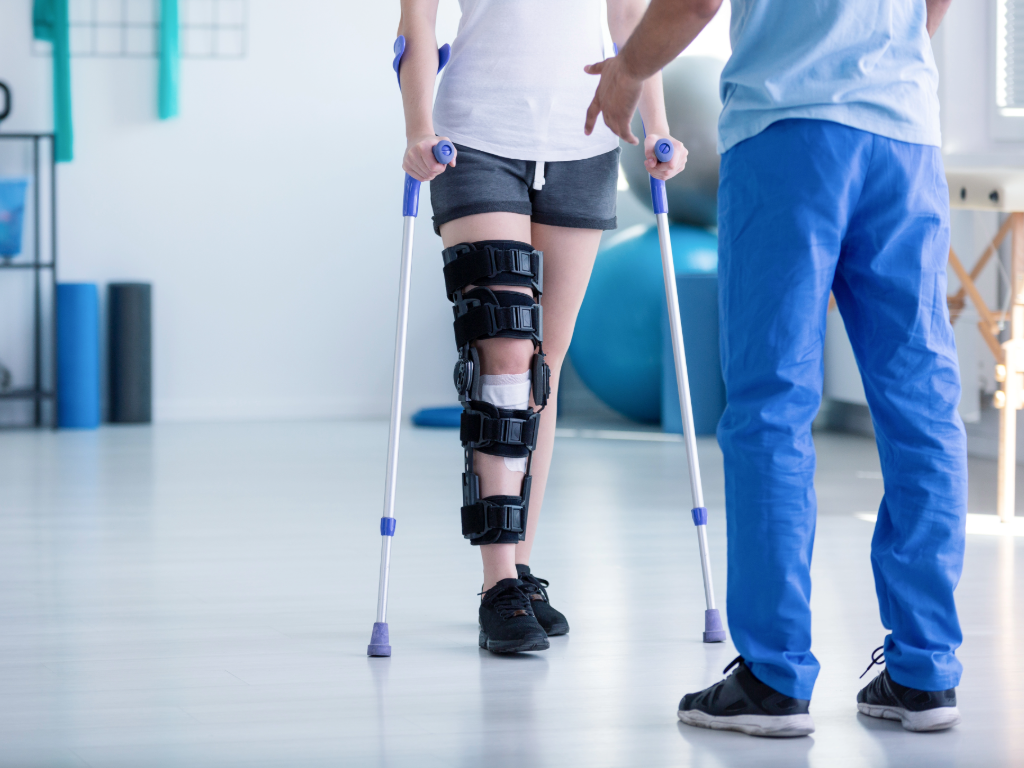 Physical therapy being shown as a person wearing a knee brace walks toward therapist on crutches.