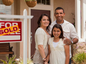 Family of 3 standing in front of their new home with a sold sign behind them for article Protecting Your Investment: Texas Homestead Laws for newcomers moving to Austin.