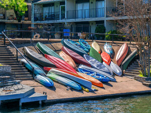 Bunch of different color kayaks and canoes pulled up on ramp in front of apartment building for article 5 Unforgettable Outdoor Adventures in Austin for Newcomers moving to Austin.