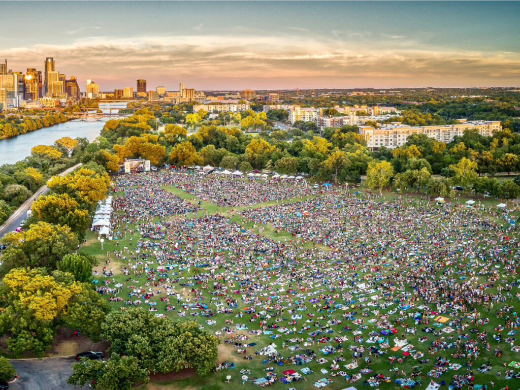 Bird's eye view of music festival in Austin's park with thousands of people out on the grass and the city of Austin in the background for article The Live Music Capital of the World: A Newcomer's Guide to Austin, Texas for newcomers moving to Austin.