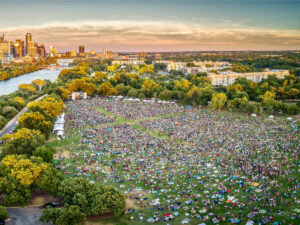 Bird's eye view of music festival in Austin's park with thousands of people out on the grass and the city of Austin in the background for article The Live Music Capital of the World: A Newcomer's Guide to Austin, Texas for newcomers moving to Austin.