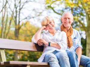 Senior man with arm around senior woman both in jeans sitting on park bench outdoors for article 9 Best Austin Neighborhoods for Retirement for newcomers retiring in Austin.