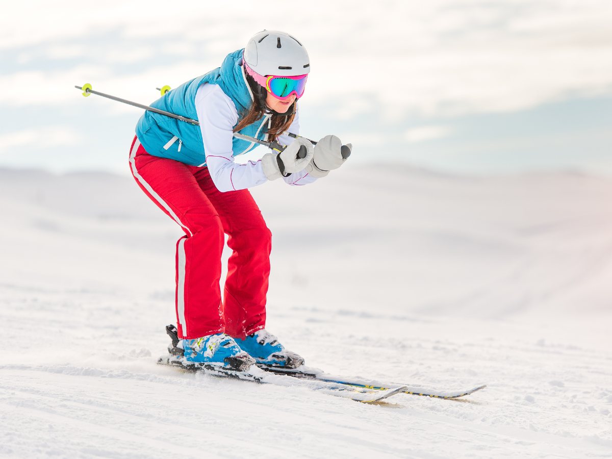 Image of a beginner snow skier with red snow pants and blue vest, helmet and goggles who is slowly skiing on a slight downhill for article Snow Ski Near Austin: 5 Popular Options for newcomers moving to Austin.
