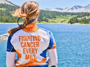 Back of girl looking out over lake with mountains in backgound and a shirt on that says fighting cancer every mile for article Texas 4000 for Cancer: Austin’s Epic Ride of Hope and Impact for newcomers moving to Austin.