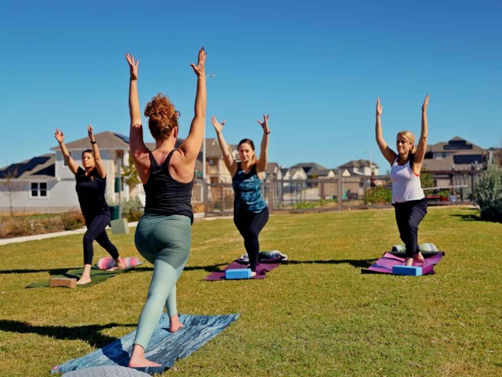 4 People doing yoga in an open outdoor area for article Whisper Valley Leads the Way in Sustainable Living in East Austin for newcomers moving to Austin.