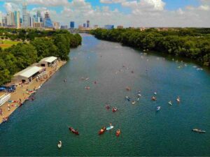 Aerial view of water with lots of paddleboarders and kayakers on the water and Austin skyline in the background for article Paddleboarding and Kayaking in Austin: 9 Must-Try Spots for Fun for newcomers moving to Austin.