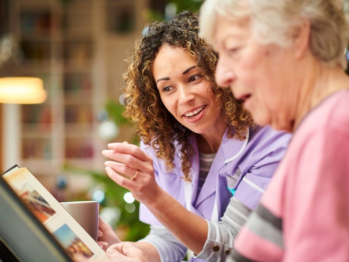 Younger woman helping an elderly woman as they look at pictures for article Alzheimer's and Dementia Care in Austin for newcomers moving to Austin or within the Austin area.