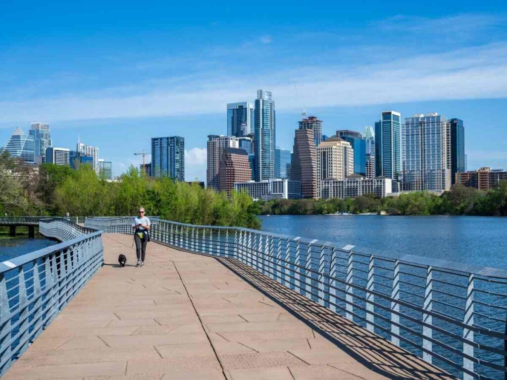 Person on walking bridge over lake with Austin skyline in background for article Why Move to Austin? for newcomers moving to Austin.